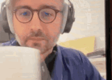 a man wearing glasses and headphones is drinking from a mug .