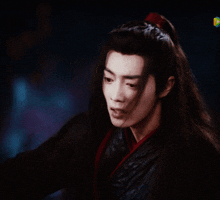 a man with long black hair and a red ribbon in his hair looks at something