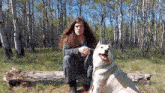 a man with long hair sits on a log with a dog