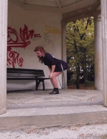 a woman is squatting down in front of a wall with graffiti that says " s.m.r. "
