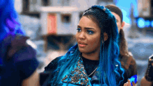a woman with blue hair and braids is standing next to a group of people .
