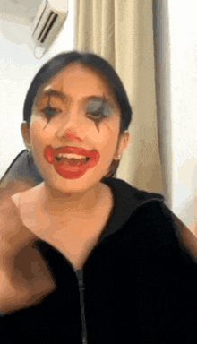 a woman with clown makeup on her face is sitting in a room .