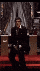 a man in a suit sits on a red carpet with the words say hello to my little ganges