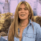 a woman with long blonde hair is wearing a denim shirt and a gold necklace