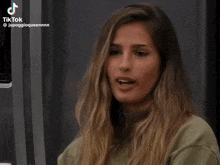 a woman with long blonde hair is wearing a green sweater