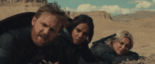a man with a beard and two women laying on the ground with guns