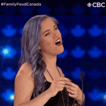 a woman with blue hair is singing into a microphone with a cbs logo in the background