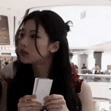 a woman with long black hair is holding a piece of paper .