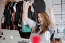 a woman is sitting at a desk with her arms in the air in front of a laptop computer .