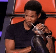 a man is drinking water through a straw while sitting in a red chair .
