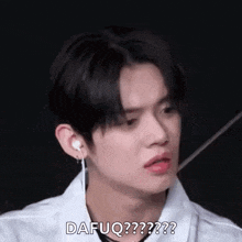 a young man wearing ear buds and a white shirt is making a surprised face .