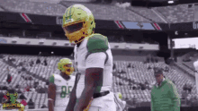 a football player wearing a green and yellow helmet is standing on a field in front of a stadium .