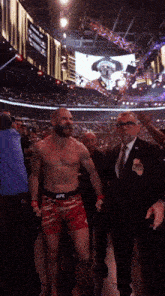 a man in a suit and tie walks with a shirtless fighter in a ufc ring