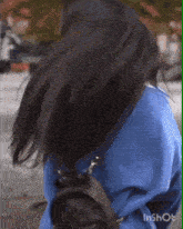 a woman wearing a blue sweater and a black backpack is blowing her hair in the wind .