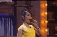 a woman in a yellow shirt is singing into a microphone on a tv show .