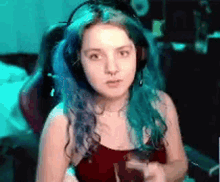 a girl with blue hair is wearing headphones and a red top .