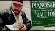 a man standing in front of a green sign that says pianos & r