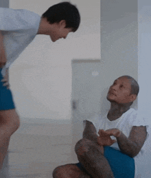 two men are talking to each other in a room . one of the men is sitting on the floor and the other is standing .