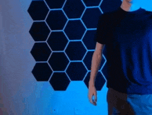 a man in a blue shirt is standing in front of a wall with a pattern of hexagons on it .