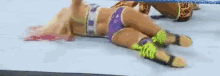 a woman is laying on the ground in a wrestling ring while another woman is kneeling on the ground .