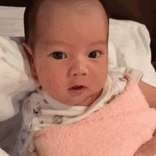 a baby is wrapped in a pink blanket and looks at the camera