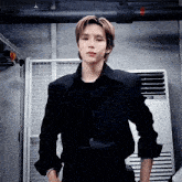a young man in a black shirt is standing in front of an air conditioner and looking at the camera