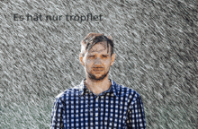 a man in a plaid shirt stands in the rain with the words es hat nur troplet above him