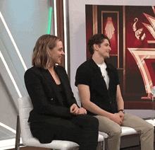 a man and a woman sit next to each other in front of a red wall