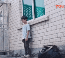 a boy leaning against a brick wall with a sign that says you on it