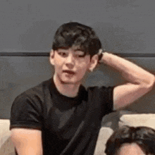 a young man in a black shirt is sitting on a couch with his hand behind his head .