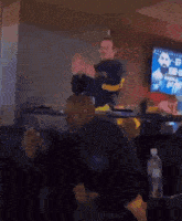 a man wearing a nike sweatshirt applauds in front of a television