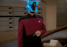 a man in a star trek uniform with a blue cube on his head holding a pen