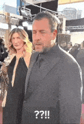 a man in a suit and tie is standing next to a woman on a red carpet with a question mark on the bottom