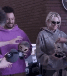 a man in a purple hoodie is standing next to a woman in a grey hoodie holding a stuffed animal .