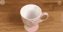 a pink and white cup with a heart on the handle is sitting on a wooden table .