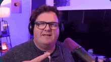 a man wearing headphones and glasses is standing in front of a microphone in a room .