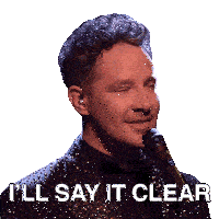 a man in a suit singing into a microphone with the words " i 'll say it clear " below him