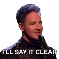 a man in a suit singing into a microphone with the words " i 'll say it clear " below him