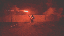 a man is holding a red flare in front of a wall that says the maw