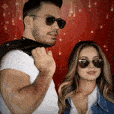a man and a woman wearing sunglasses are standing next to each other in front of a red background
