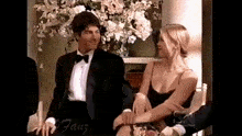 a man in a tuxedo sits next to a woman in a black dress .