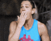 a woman wearing a blue kappa tank top covering her mouth