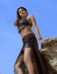 a woman is standing on a rock wearing a crop top and a high slit skirt .