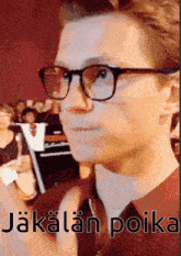 a man wearing glasses and a red shirt with the words " jokalan poika " on the bottom right