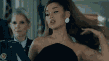 ariana grande is wearing a black strapless dress and earrings while holding her hair .