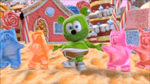 a gummy bear is dancing with other gummy bears in front of a gingerbread house