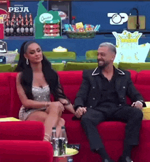 a man and a woman are sitting on a red couch holding hands and smiling .