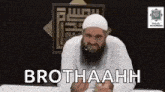 a man with a beard and a white hat is sitting at a table with a microphone .