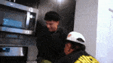 two men are standing in front of a microwave with one wearing a white hat with the letter g on it ..